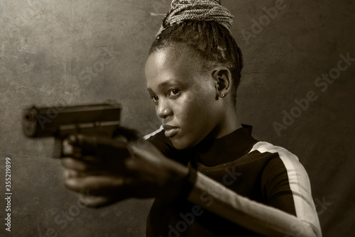 Hollywood movie style portrait of young attractive and confident black African American woman holding gun as special federal agent or mobster pointing the handgun