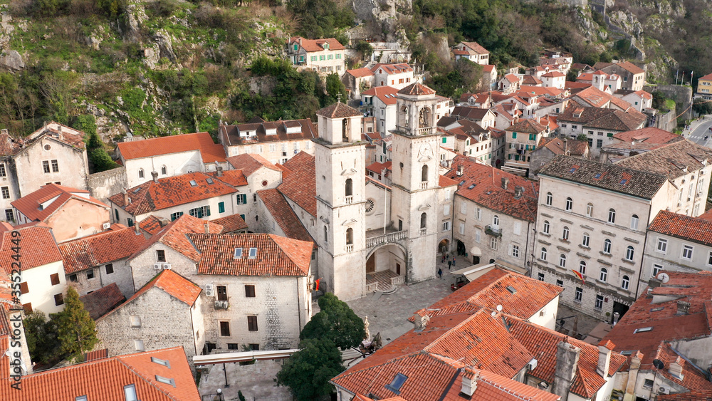 Kotor medieval old town and major tourist destination in Montenegro, featuring The Cathedral of Saint Tryphon from 12th century. Aerial view of vintage stone houses with red roofs, on a sunny day.