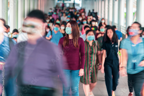 Asian woman walking and standing between Crowd of blurred unrecognizable business people wearing surgical mask