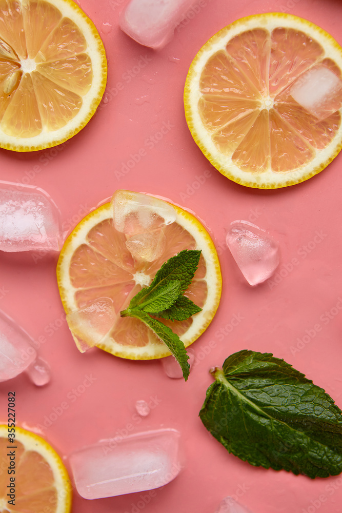 Composition with cut citrus fruits on pink background. Creative summer background composition with lemon slices, leaves mint and ice cubes. Minimal top down lemonade drink concept.Top view Composition with cut citrus fruits on pink background. Creative summer background composition with lemon slices, leaves mint and ice cubes. Minimal top down lemonade drink concept.Top view