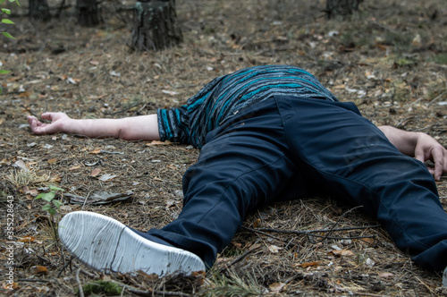 Murder in the woods. The body of a man in a blue t-shirt and trousers lies on the ground among the trees in the forest. Victim of an attack.