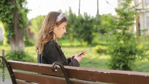 Beautiful girl is sitting in the park with her phone in hands.