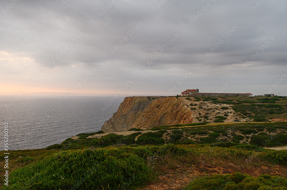 Old church in Portugal on a hill by the ocean at sunset.