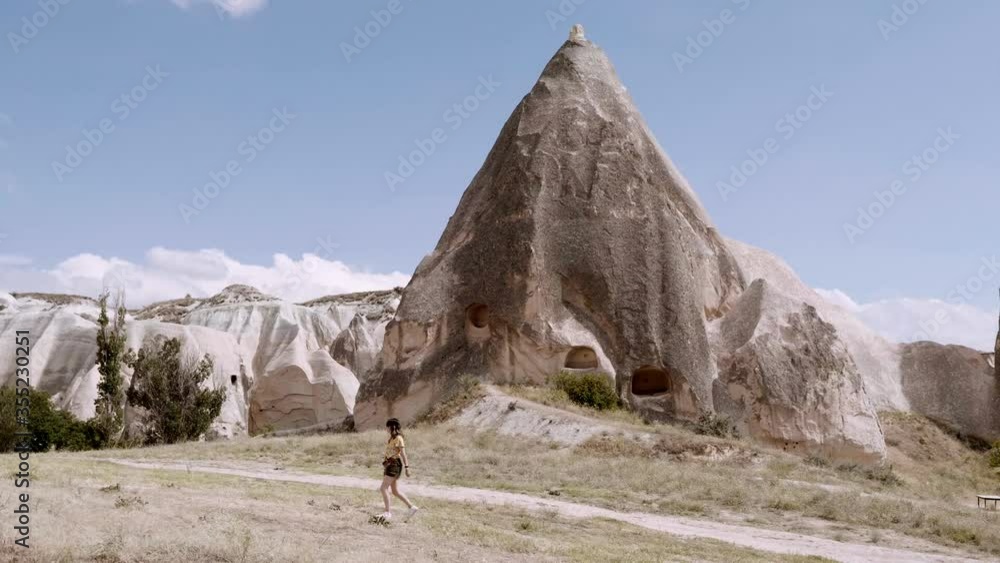 Woman walking through the countryside in front of a cave in the Turkish Capadoccia Woman walking through the countryside in front of a cave in the Turkish Capadoccia