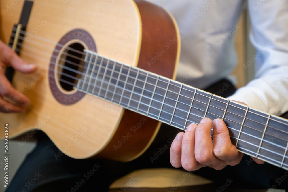 Fototapeta premium Classical guitar - Guitarist playing acoustic guitar in studio - selective focus close-up of the fingerboard and hand