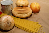 apple, spaghetti, onions, bread and canned goods lie on a paper bag