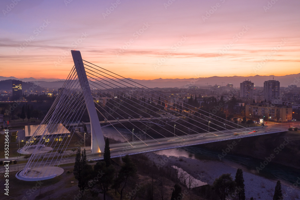 Podgorica Montenegro - city lights and orange and purple sky in the evening, after sunset. Cable-stayed Millennium bridge over river Moraca, at night.
