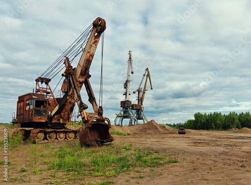 old heavy machinery, in the form of a huge excavator and high cranes, on a sand quarry against a beautiful blue cloudy sky