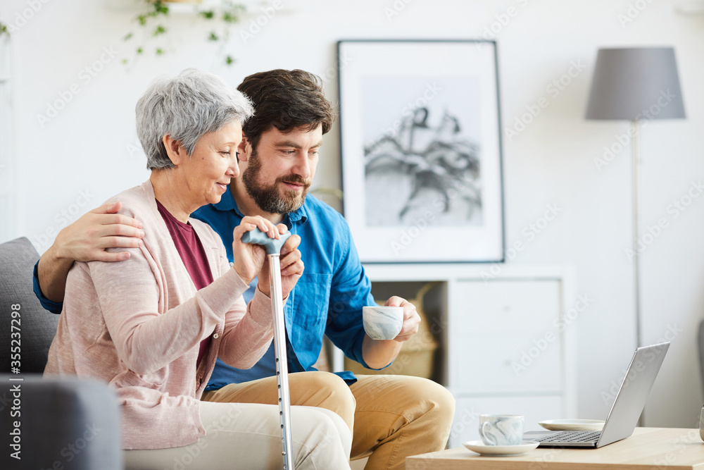 Obraz premium Family of two sitting on the sofa and looking at monitor of laptop they have online conversation at home