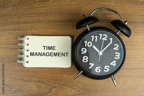 alarm clock on wooden table with TIME MANAGEMENT word photo