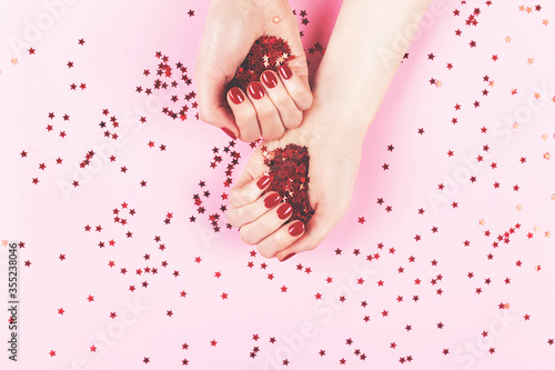 Manicure and nailcare concept. Two woman hands holding confetti on pink background. Flat-lay, top view. Copy space. photo