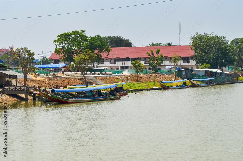 Rural riverside of Chao Phraya river with traditional thai transit boats next to cable car station for river crossing 