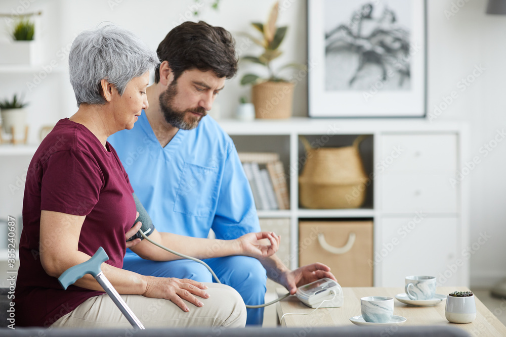 Mature male doctor examining the blood pressure of senior woman while they sitting on sofa at home Mature male doctor examining the blood pressure of senior woman while they sitting on sofa at home
