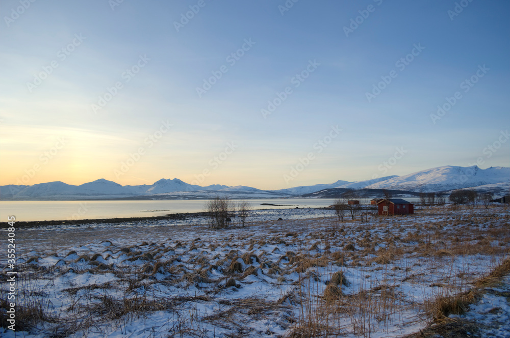 long field with small red buildings and mountain backdrop