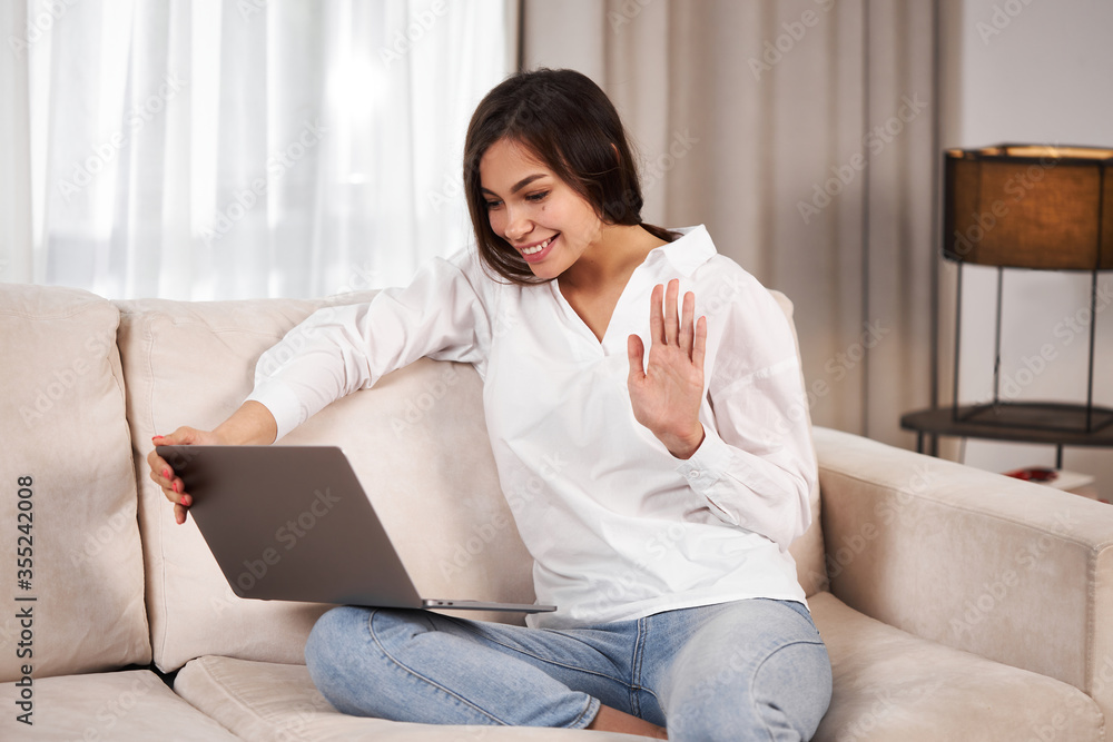 Naklejka premium Young girl with a laptop. A young girl with a laptop is talking via video call. Portable electronics at home