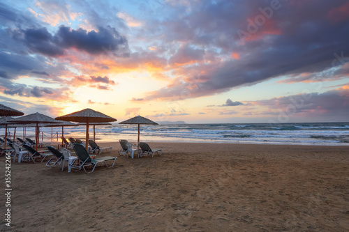 Empty beach with umbrellas and deck chairs closed. Unbelievable sunrise. 2020 summer quarantine travel. Beautiful summertime view seascape. Relax places island Crete  Greece.