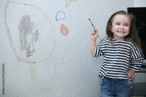 The child outlined the wall, holds a brush in his hands and laughs. Unattended child. The child paints with watercolors on the wall, until his parents see. 