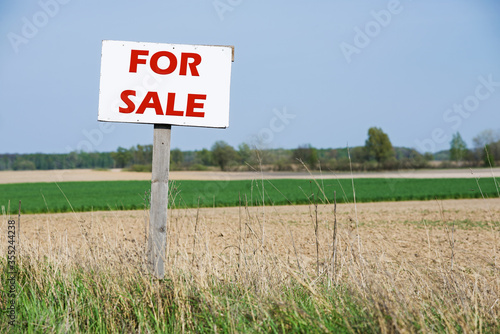A sign is in front of the agricultural field. For sale. Red text.