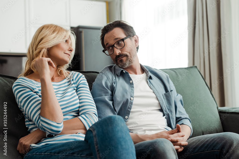 Selective focus of handsome mature man looking at beautiful wife on sofa Selective focus of handsome mature man looking at beautiful wife on sofa