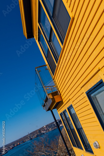 The side exterior wall of a bright yellow wooden clapboard building with closed windows and a glass patio. The bright blue sky is in the background. The house is a multiple storey building. 