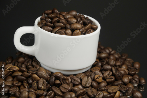 White mug with coffee grains sprinkled with coffee grains on a background