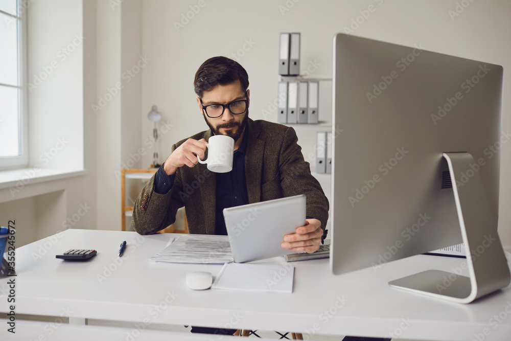 Businessman worker drinking a coffee mug while sitting at a table with a computer working in the office. Businessman worker drinking a coffee mug while sitting at a table with a computer working in the office.