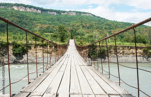 old wooden bridge across mountain river in Adygea. Footpath on trekking route in scenic touristic places. Traveling concept.