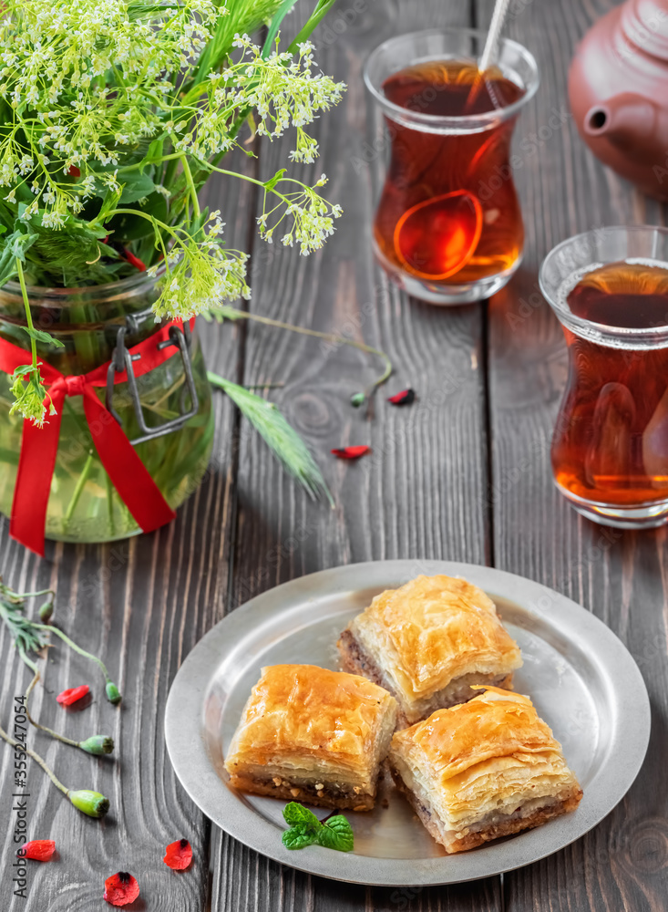 Turkish (eastern) dessert Ramadan Baklava with walnuts and hazelnuts, black strong Turkish tea in a glass of armudu (boomaly). Close-up, shallow depth of field, spring still life Turkish (eastern) dessert Ramadan Baklava with walnuts and hazelnuts, black strong Turkish tea in a glass of armudu (boomaly). Close-up, shallow depth of field, spring still life