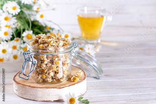 Dried chamomile in the jar on the wooden table. Organic Chamomile Tea in cup and flowers. Copy space photo