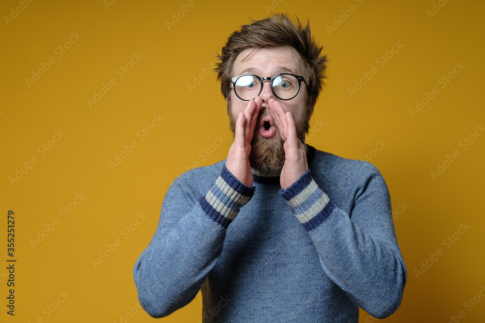 Man with a shaggy hairstyle and a beard with hands on lips whispers gossip and rumors. Copy space. Man with a shaggy hairstyle and a beard with hands on lips whispers gossip and rumors. Copy space.