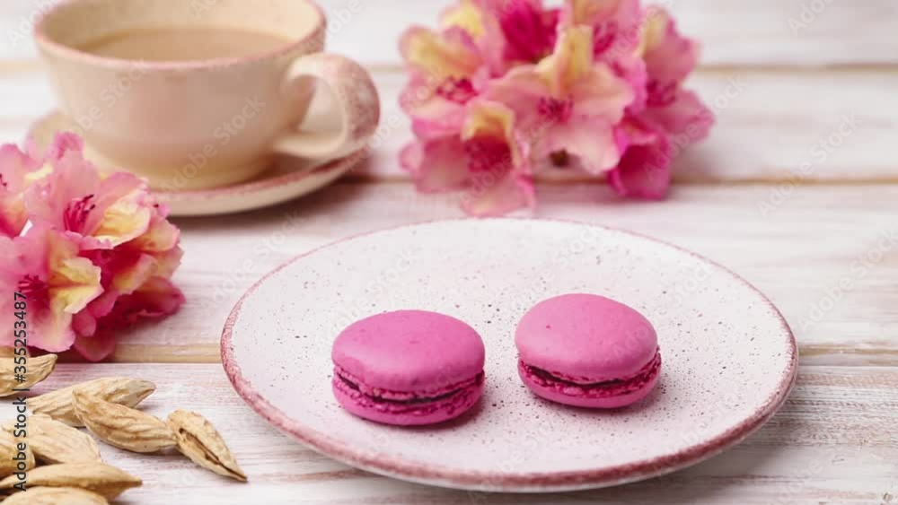 male hand puts pink macaroons on a ceramic plate on a white wooden background. Side view, close up. male hand puts pink macaroons on a ceramic plate on a white wooden background. Side view, close up.