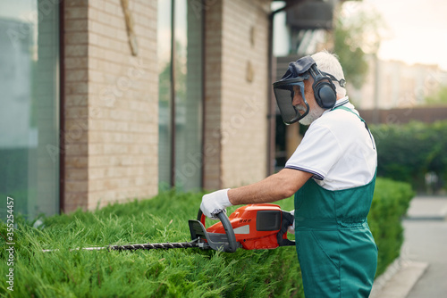 Man wearing ear and face defenders cutting bushes.