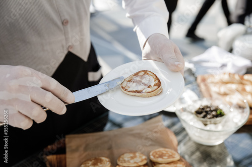 The waiter smears the pancake with butter on a white plate.