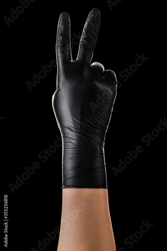 Hand in black gloves showing two fingers up in peace or victory symbol on black