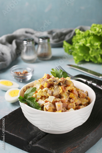 Salad with ham, eggs, onion and mushrooms in a white bowl on black wooden board, Vertical format, Closeup