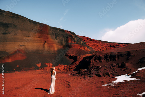 The girl is standing with her back. Portrait of a bride model in a golden wedding evening dress, in a yellow-red sandy quarry, in the crater of a volcano in Iceland, Golden Circle.