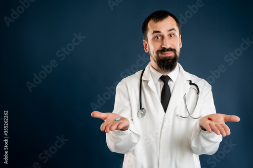 Male doctor with stethoscope in medical uniform showing red and blue pills on hands
