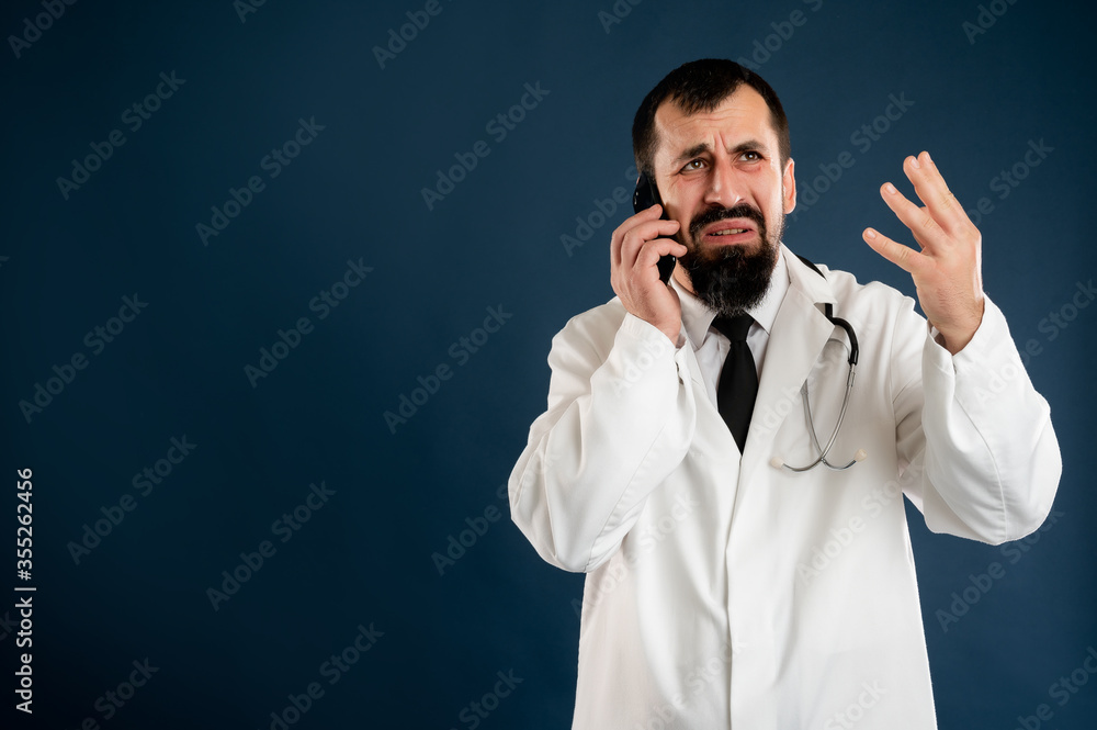Male doctor with stethoscope in medical uniform displeased face and gestures and talking on cellphone Male doctor with stethoscope in medical uniform displeased face and gestures and talking on cellphone