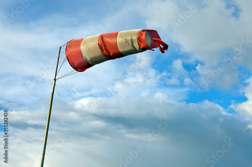 Meteorology wind bag for marine navigation. Red and white windsock blows against a blue sky