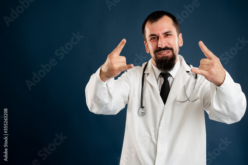 Male doctor with stethoscope in medical uniform doing rock symbol with hands up