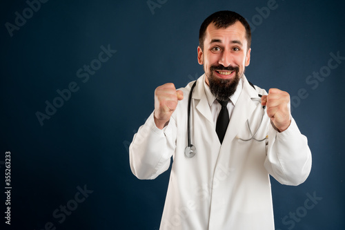 Male doctor with stethoscope in medical uniform raised fists up exclaiming with joy and excitement