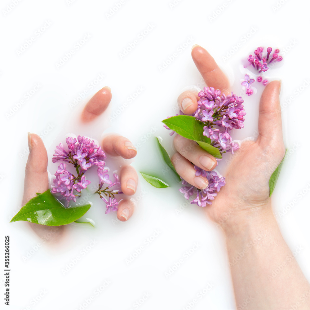 The palms of a girl in a bath with milk and flowers. Lilac flowers. Copy space, flat lay. The concept of purity, tenderness, freshness, youth.