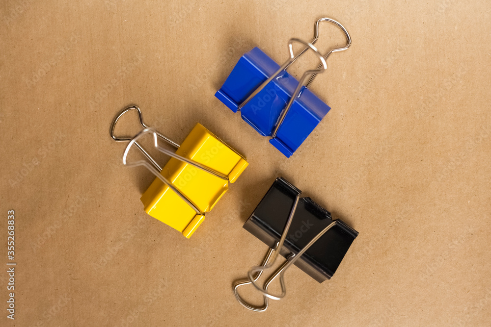Three colored paper clips on a brown background. Top view. Background, craft paper