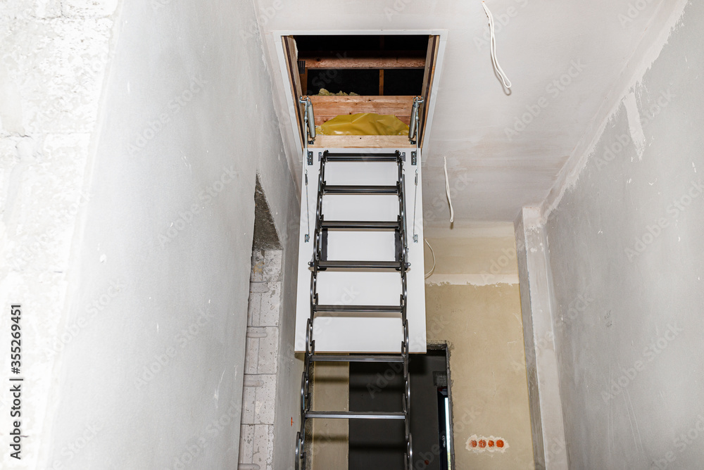 Fototapeta premium Sliding metal stairs to the attic in the ceiling, open flap and unfolded stairs, modern look.