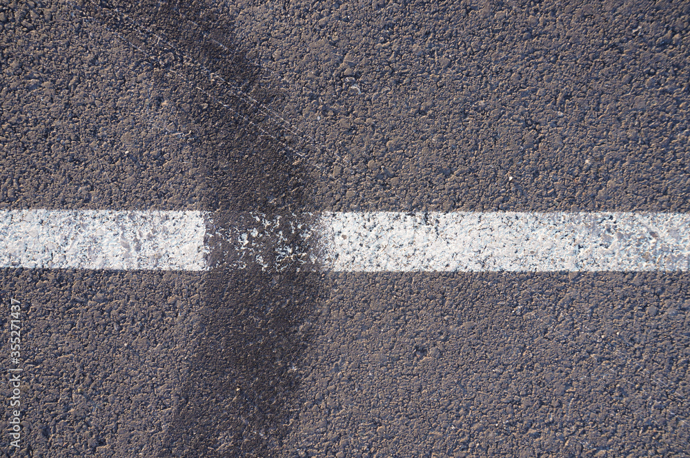 Fototapeta premium Asphalt texture with white line and tire marks. Smooth asphalt road. Tarmac dark grey grainy road background.Top view