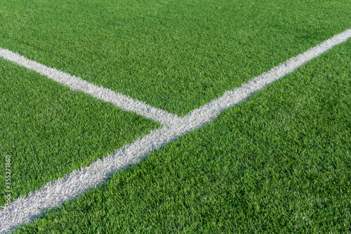 Green grass and white border lines on football ground. Soccer field on artificial turf. Artificial green grass texture. Artificial football field in an open stadium