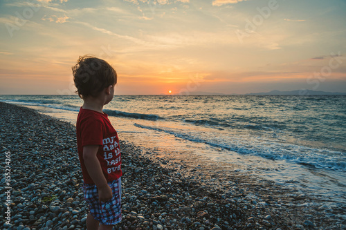 Small boy on pebble beach during sunset. West coast of Island of Rhodes. Greece.