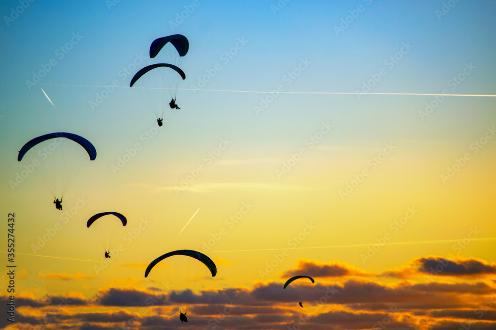 silhouettes of a paragliders flying in the sky at bright and cloudy sunset. Paragliding sport concept