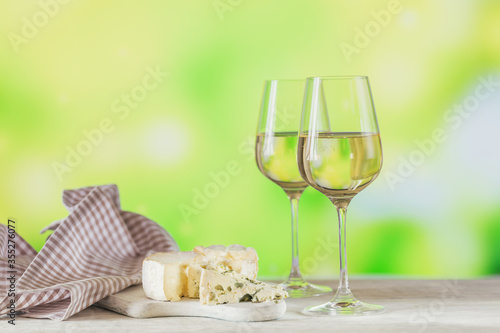 Two glasses of white wine served with cheese board on light green background. Wine mood concept