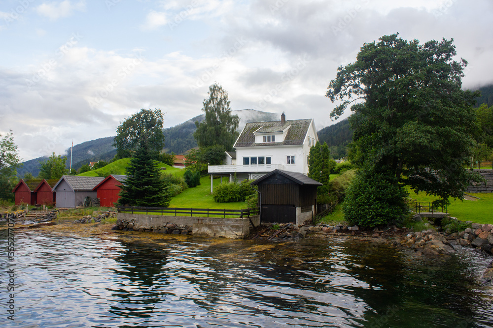 Obraz premium Small wooden boat garages and a white house on the fjord. Balestrand. Norway
